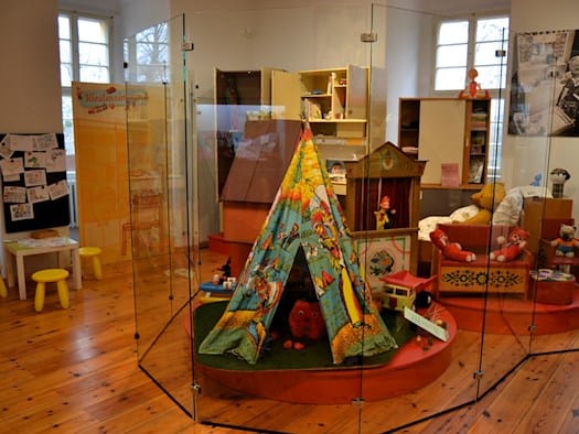 Ein Tipi-Zelt, ein Kaspertheater und anderes DDR-Spielzeug hinter Glas in einer Ausstellung über DDR-Kinderzimmer.