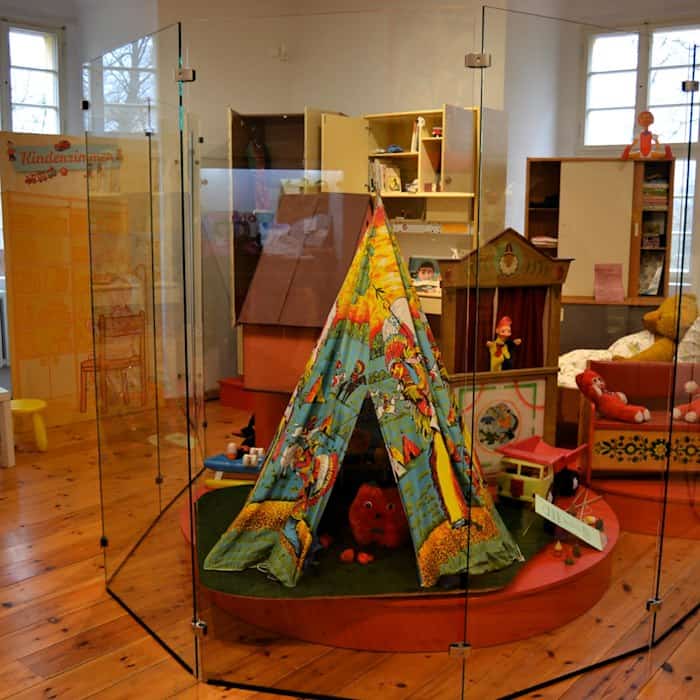 Ein Tipi-Zelt, ein Kaspertheater und anderes DDR-Spielzeug hinter Glas in einer Ausstellung über DDR-Kinderzimmer.