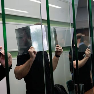 Angeklagte verdecken ihre Gesichter im Gerichtssaal beim Prozess wegen mehrerer Fahrzeugbrände. (Archivbild)  / Foto: Carsten Koall/dpa