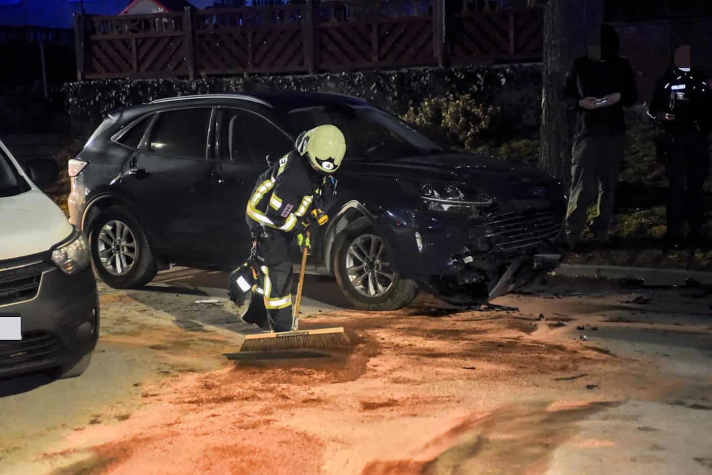 Feuerwehrmann in Schutzkleidung kehrt vor einem beschädigten schwarzen SUV auf einer Straße bei Nacht