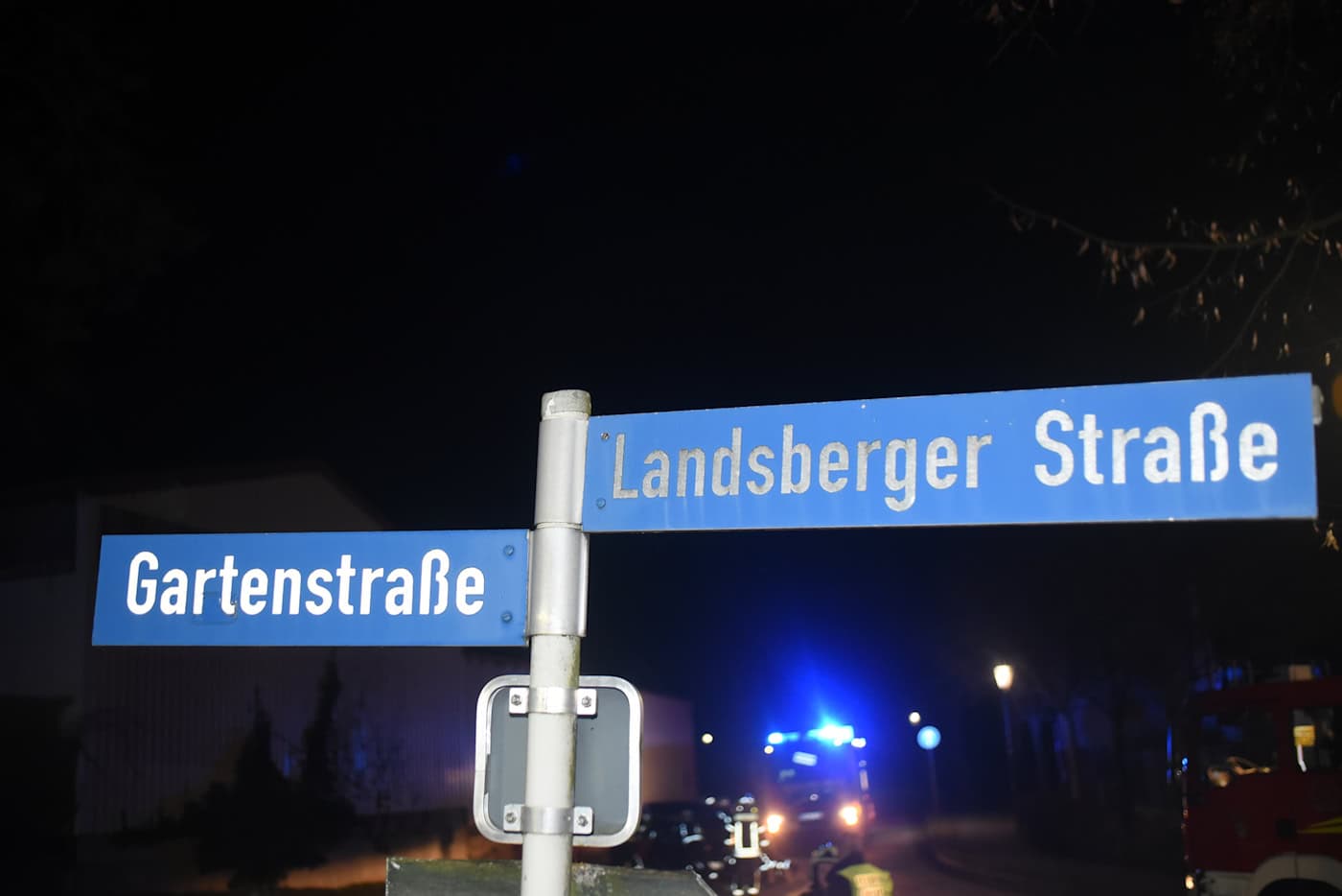 Straßenschilder für Gartenstraße und Landsberger Straße bei Nacht mit Blaulicht im Hintergrund