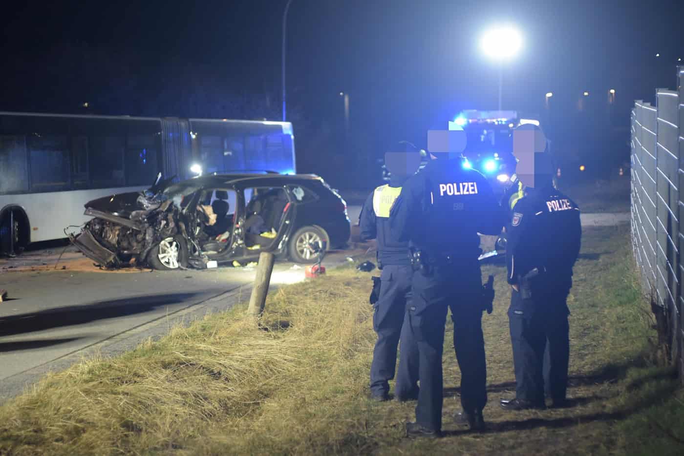 Unfallstelle bei Nacht mit stark beschädigtem Auto, mehreren Polizisten und einem Bus im Hintergrund