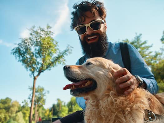 Lächelnder Mann streichelt glücklichen Golden Retriever im Freien.
