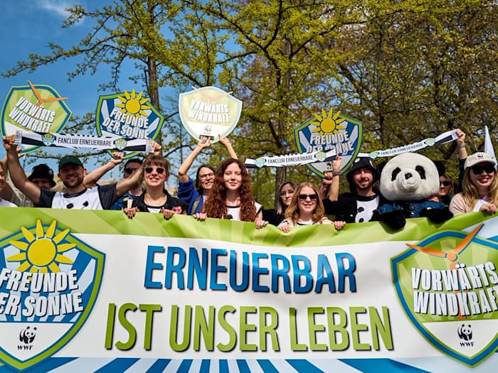 Demonstrierende halten ein Banner und Schilder in die Höhe, darunter eine Person im Pandakostüm. / Foto: Michael Ukas/dpa