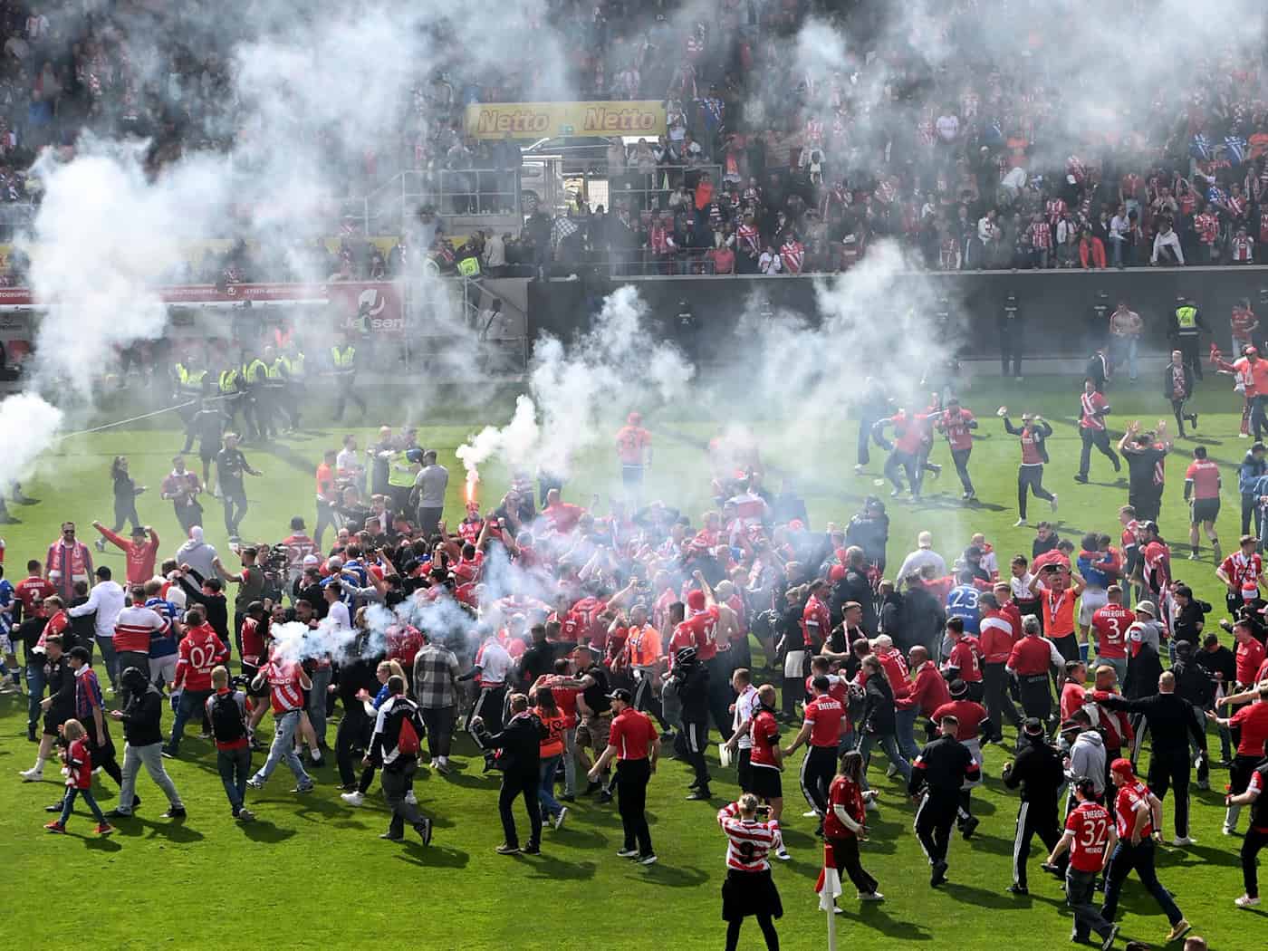 Aufstiegsfeier mit Pyrotechnik: Fans des FC Energie Cottbus auf dem Spielfeld in Regensburg. / Foto: Jens Niering/dpa
