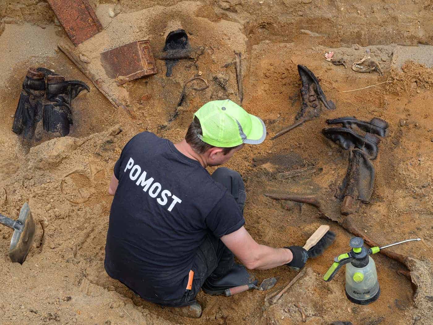 Ein bislang verborgenes Grab mit Kriegstoten in Westpolen: Ein Mitglied des Vereins Pomost legt die Gebeine und andere Funde wie Stiefel frei.  / Foto: Patrick Pleul/dpa