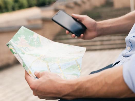 Eine Person hält eine Landkarte in der Hand und nutzt gleichzeitig ein Smartphone.