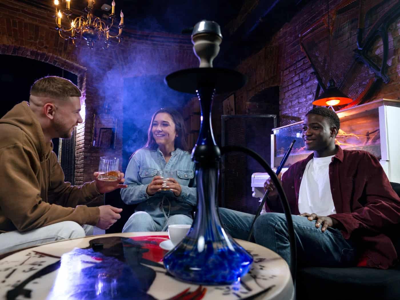 Drei Freunde in gemütlicher Runde mit einer Shisha in einem rustikalen Raum mit Ziegelwänden