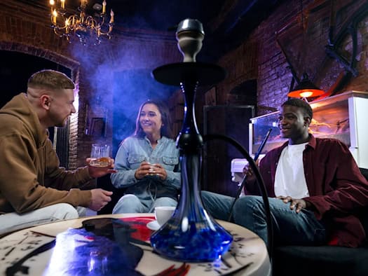 Drei Freunde in gemütlicher Runde mit einer Shisha in einem rustikalen Raum mit Ziegelwänden