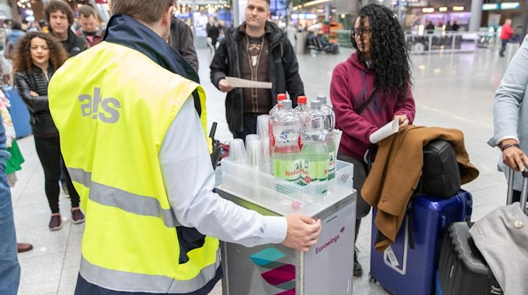 Ein Mitarbeiter verteilt Getränke und gibt Informationen an gestrandete Fluggäste. Foto: Friso Gentsch/dpa