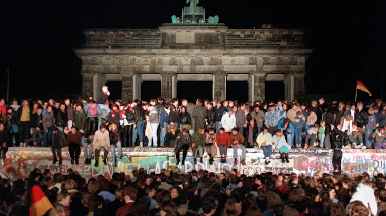 Jubelnde Menschen auf der Berliner Mauer am Brandenburger Tor 1989. Foto: Wolfgang Kumm/dpa/Archivbild