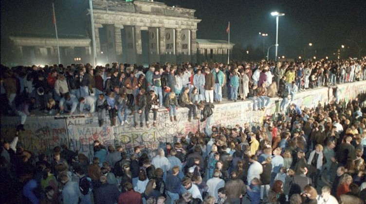 Menschen auf der Berliner Mauer vor dem Brandenburger Tor in der Nacht vom 9. auf den 10.11.1989. Foto: Peter Kneffel/dpa