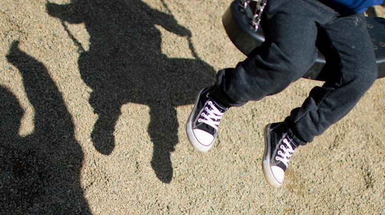 Der Schatten von einem Mann und einem schaukelnden Kind fällt auf einen Spielplatz. Foto: Julian Stratenschulte/dpa/Archivbild