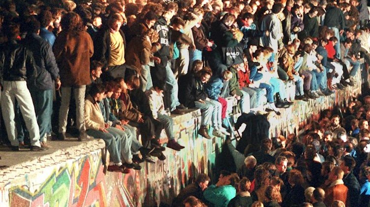 Jubelnde Menschen sitzen mit Wunderkerzen auf der Berliner Mauer am 11.11.1989. Foto: dpa