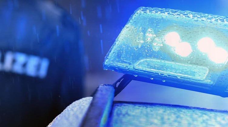 Ein Polizist steht im Regen vor einem Streifenwagen dessen Blaulicht aktiviert ist. Foto: Karl-Josef Hildenbrand/dpa