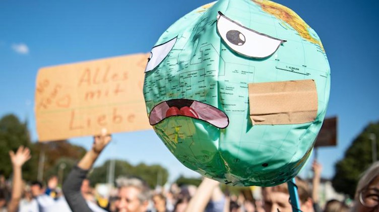 Demonstranten halten einen Luftballon mit Globusaufdruck hoch, der mit einem Pflaster und unglücklichen Gesichtszügen beklebt ist. Foto: Sina Schuldt/Archiv