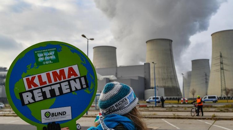 Eine Umweltschutzaktivistin vor den dampfenden Kühltürmen des Braunkohlekraftwerkes Jänschwalde. Foto: Patrick Pleul/dpa-Zentralbild/dpa