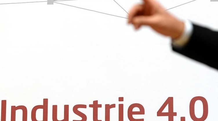 Auf einem Schild steht "Industrie 4.0", während ein Redner seinen Zeigefinger hebt. Foto: Ralf Hirschberger/dpa-Zentralbild/dpa/Archivbild
