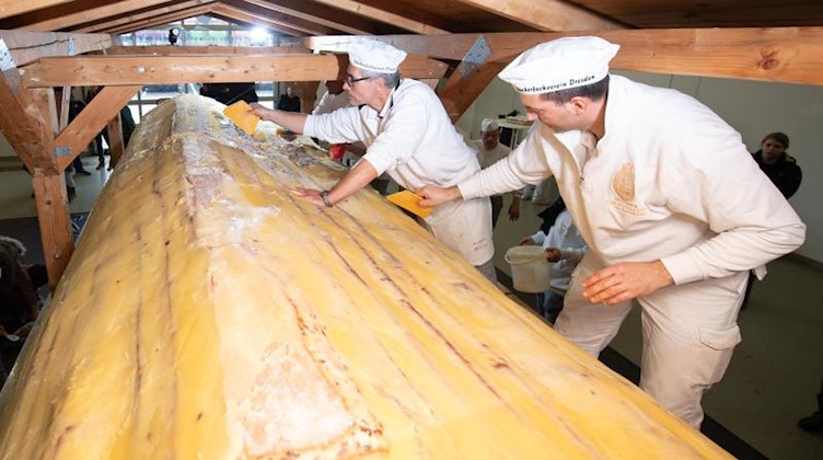 Bäcker der Schutzgemeinschaft Dresdner Stollen streichen Butter und Zucker auf den Riesenstollen. Foto: Sebastian Kahnert/dpa-Zentralbild/dpa