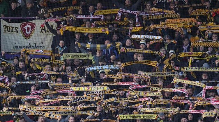 Fans aus Dresden halten ihre Schals nach oben. Foto: Friso Gentsch/dpa