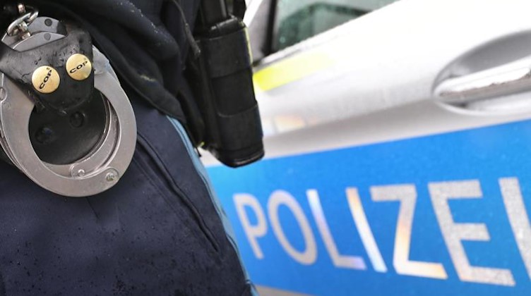 Ein Polizist mit Handschellen und einer Pistole am Gürtel steht vor einem Streifenwagen. Foto: Karl-Josef Hildenbrand/dpa