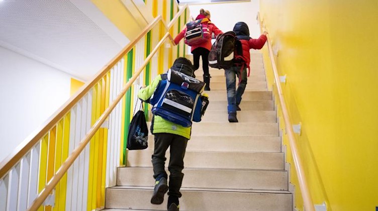 Grundschulkinder laufen mit ihren Schulranzen und Turnbeuteln über eine Treppe in ihr Klassenzimmer. Foto: Christian Charisius/dpa