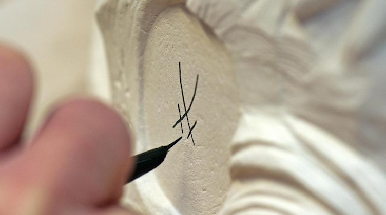 Eine Person zeichnet das Markenzeichen der Porzellan Manufaktur Meissen auf einen Rohling. Foto: Arno Burgi/zb/dpa/Archivbild
