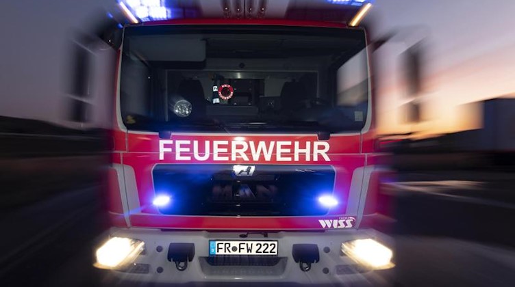 Ein Feuerwehrfahrzeug steht mit eingeschaltetem Blaulicht im Sonnenuntergang auf einer Straße. Foto: Patrick Seeger/dpa