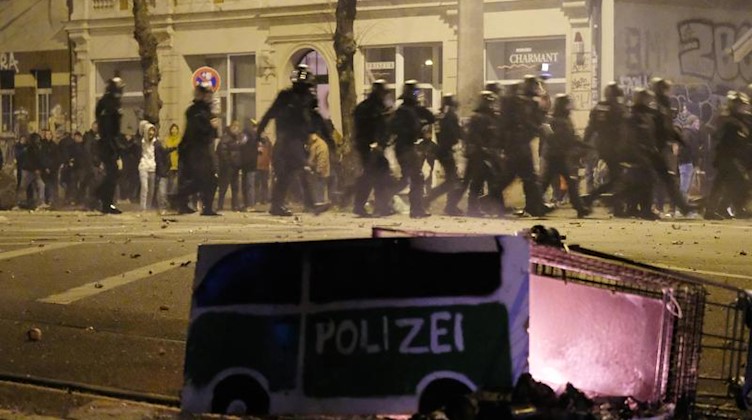 Polizisten räumen eine Kreuzung im Stadtteil Connewitz, während im Vordergrund ein Einkaufswagen liegt. Foto: Sebastian Willnow/dpa-Zentralbild/dpa