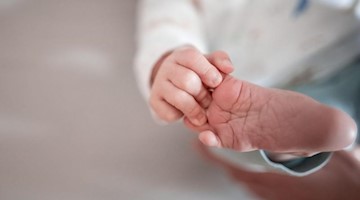 Ein Baby greift mit den Fingern nach seinem Fuß. Foto: Fabian Strauch/dpa