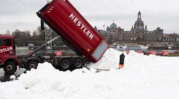 Ein LKW kippt am Elbufer vor der Frauenkirche eine Ladung Kunstschnee auf eine künftige Wettkampfstrecke. Foto: Sebastian Kahnert/dpa-Zentralbild/dpa