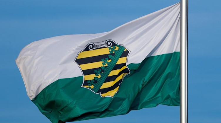 Die Flagge vom Bundesland Sachsen mit dem sächsischen Wappen weht im Wind. Foto: Monika Skolimowska/zb/dpa/Archivbild