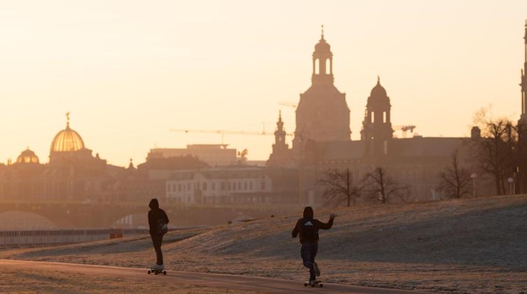 Zwei Skateboarder fahren bei Sonnenaufgang vor der Kulisse der Altstadt am Ufer der Elbe entlang. Foto: Sebastian Kahnert/dpa-Zentralbild/dpa/Archivbild