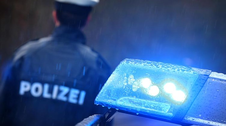 Ein Polizist steht im Regen vor einem Streifenwagen dessen Blaulicht aktiviert ist. Foto: Karl-Josef Hildenbrand/Archiv