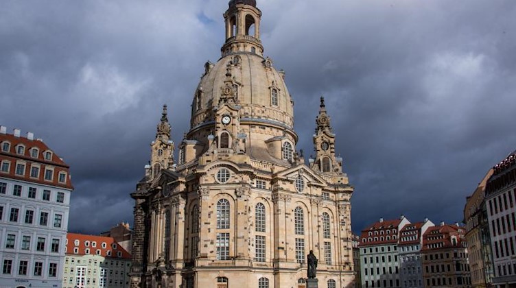 Die Frauenkirche wird vor einer dunklen Wolkenkulisse von der Wintersonne angestrahlt. Foto: Jens Büttner/dpa-Zentralbild/dpa/Archivbild