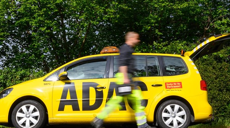 Ein Pannenhelfer vom ADAC geht an seinem Auto mit einer Autobatterie in der Hand vorbei. Foto: Christophe Gateau/dpa/Archivbild