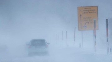 Autos fahren durch aufgewirbelte Schneewolken auf der Zufahrtsstraße zum Fichtelberg. Foto: Jens Büttner/dpa-Zentralbild/dpa