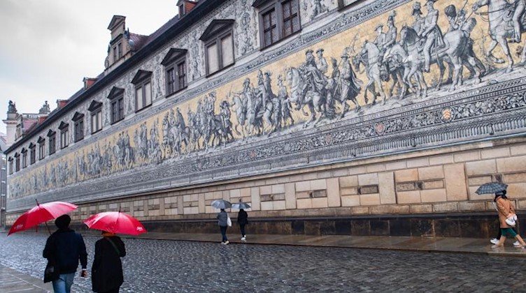 Touristen laufen bei Regen unter Schirmen am Fürstenzug entlang. Foto: Robert Michael/dpa-Zentralbild/dpa