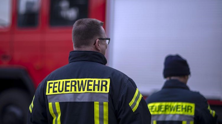 Feuerwehrmänner stehen vor einem Feuerwehrauto. Foto: Jens Büttner/zb/dpa/Archiv/Illustration