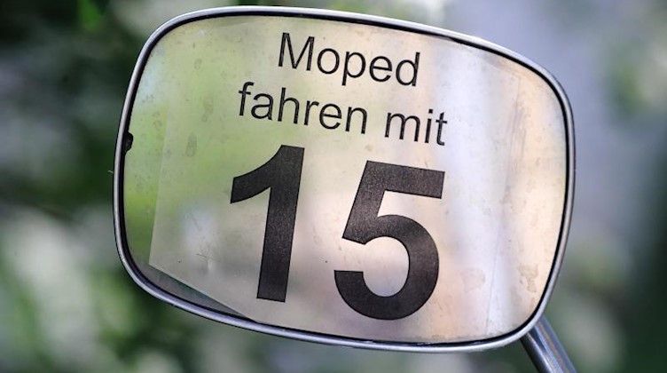 Der Schriftzug «Moped fahren mit 15» am Spiegel eines Mopeds. Foto: Jens Wolf/dpa-Zentralbild/dpa/Archivbild