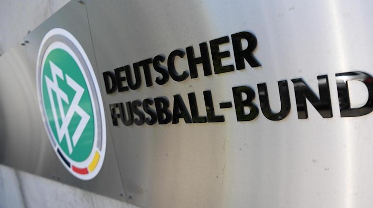 Logo und Schriftzug sind vor der Zentrale des Deutschen Fußball-Bundes (DFB) an einer Mauer platziert. Foto: Arne Dedert/dpa/Archivbild