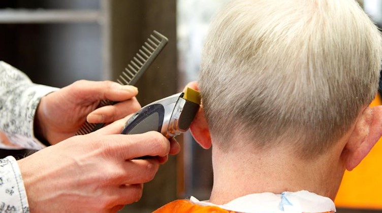 Ein Friseur schneidet einem Kunden die Haare. Foto: picture alliance / dpa/Symbolbild