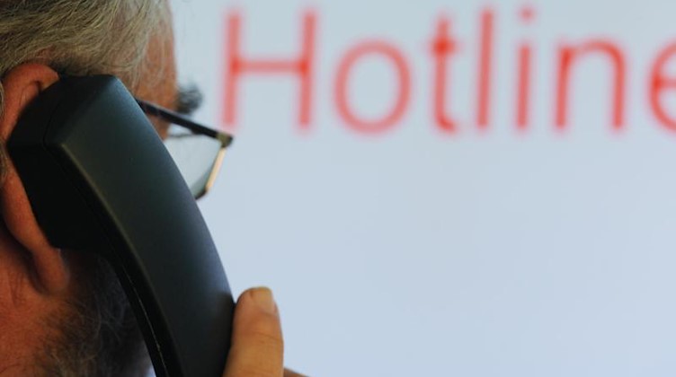 Ein Mann hält einen Telefonhörer vor dem Schriftzug «Hotline» auf einem Computermonitor. Foto: Uli Deck/dpa/Symbolbild/Illustration/Archivbild