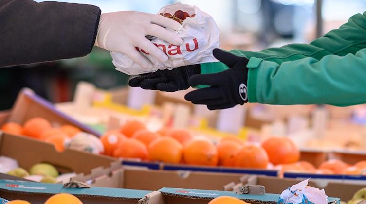 Ein Markthändler gibt mit Handschuhen eine Tüte an eine Kundin. Foto: Sebastian Gollnow/dpa