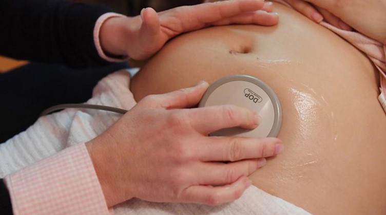 Eine Hebamme hört in einer Praxis den Bauch einer schwangeren Frau ab, um die Herztöne des Babys zu prüfen. Foto: picture alliance / Uli Deck/dpa/Archivbild