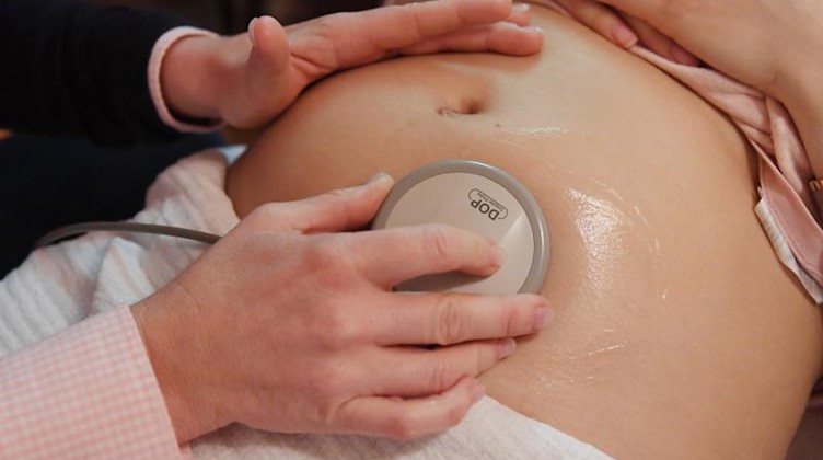 Eine Hebamme hört den Bauch einer schwangeren Frau ab, um die Herztöne des Babys zu prüfen. Foto: picture alliance/Uli Deck/dpa/Symbolbild