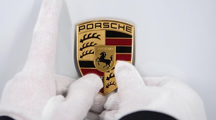 Eine Mitarbeiterin hält ein Porsche-Emblem auf eine Motorhaube. Foto: Marijan Murat/dpa/Symbolbild