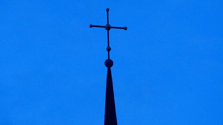 Ein Kreuz ist an einer Kirchturmspitze zu sehen. Foto: Friso Gentsch/dpa/Symbolbild