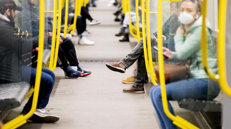 Fahrgäste sitzen in einer U-Bahn, wobei eine Frau einen Mundschutz trägt. Foto: Christoph Soeder/dpa