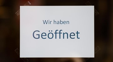 Ein Zettel mit der Aufschrift «Wir haben Geöffnet» hängt im Schaufenster eines Geschäftes. Foto: Daniel Reinhardt/dpa/Symbolbild